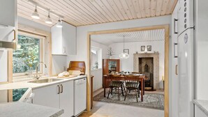 Cocina moderna con armarios de madera, horno empotrado y comedor con chimenea de ladrillo.