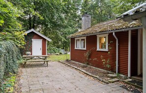 A red wooden house with a chimney, a small shed, and a picnic table in a wooded area. - Nice home in Gistrup with WiFi (Gistrup)