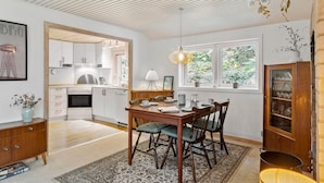 Una cocina moderna con armarios blancos, un comedor con mesa y sillas de madera, y vistas a zonas verdes a través de las ventanas.