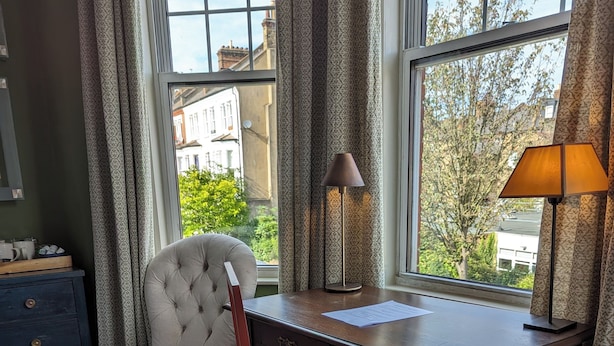 A room with a wooden desk, a chair, a lamp, and a view of buildings through a window. - 17 Trent Road  (London)