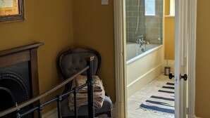 A bedroom with a bed, a chair, a fireplace, and a view of a bathroom with a bathtub. - 17 Trent Road  (London)