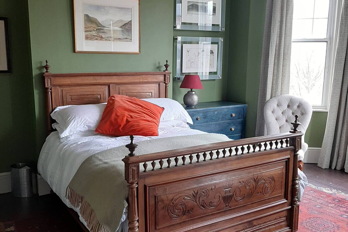 A bedroom with a wooden bed, green walls, a red rug, and a window with curtains.