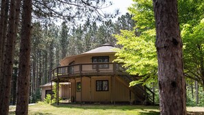 A two-story wooden cabin with a balcony, surrounded by tall pine trees.