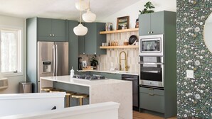 A modern kitchen with a central island, stainless steel appliances, and green cabinetry.