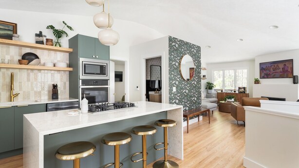 A modern kitchen with a central island, bar stools, and a dining area with a sofa and table.
