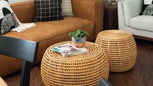 A living room with a brown sofa, two woven ottomans, a small potted plant, and a magazine on one of the ottomans.