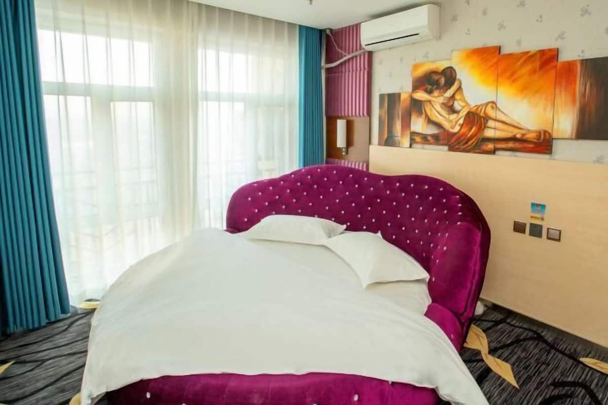 A hotel room with a large bed, a painting on the wall, and an air conditioning unit.
