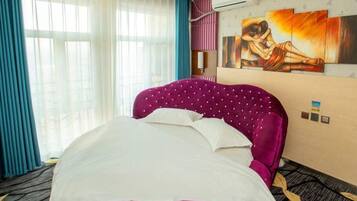A hotel room with a large bed, a painting on the wall, and an air conditioning unit.