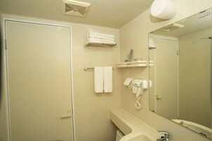 Un baño con inodoro, lavamanos, espejo, toallero y secador de pelo.