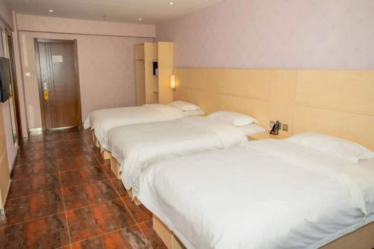 A hotel room with three beds, a television, and a tiled floor.