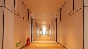 A long, narrow hotel corridor with doors on both sides, a fire extinguisher on the left, and a green exit sign. - Memo's Hotel (Manzhouli)