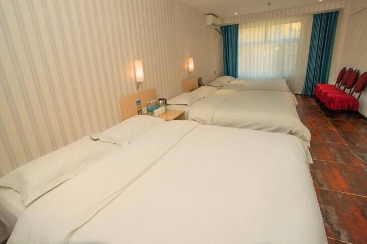 A hotel room with two beds, a small table with toiletries, a window with curtains, and a red tablecloth-covered area.