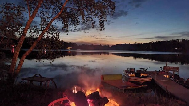 A lakeside campfire with a boat docked nearby. - Spacious cabin right on the lake, perfect for your next family vacation! (Luck)