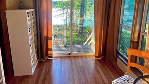 A room with a wooden floor, a white cabinet with drawers, a chair with a patterned cushion, and a large window with curtains. - Spacious cabin right on the lake, perfect for your next family vacation! (Luck)