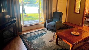 A living room with a television, a blue armchair, a wooden coffee table, and a large window with curtains. - Spacious cabin right on the lake, perfect for your next family vacation! (Luck)