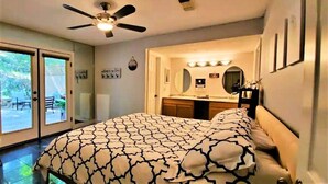 Quarto com cama, ventilador de teto, banheiro com espelho e vista para o exterior.
