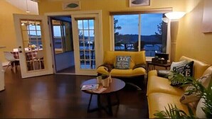 Uma sala de estar com um sofá amarelo, uma mesa de centro e uma poltrona com almofada que diz 'LIFE IS A CHALLENGE'.