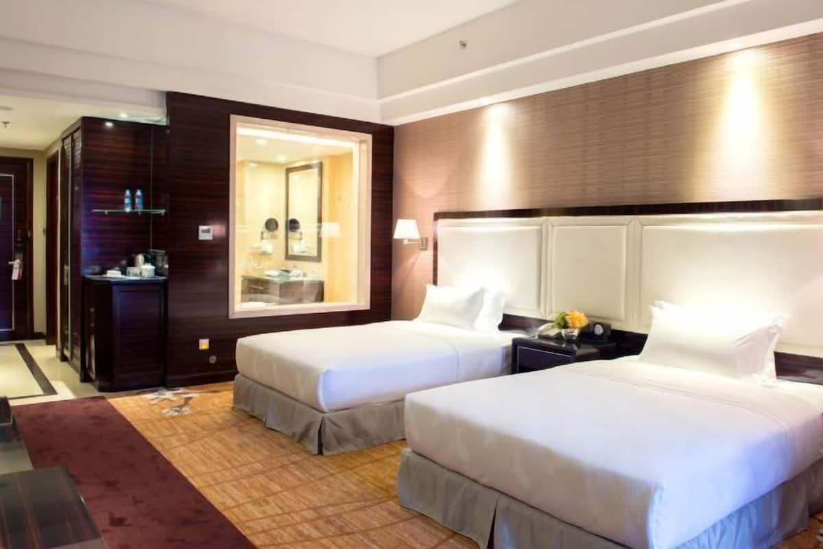 A hotel room with two beds, a large mirror, a nightstand with a lamp, and a wooden accent wall.