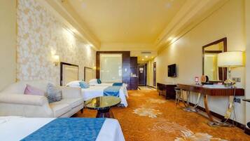 A hotel room with a sofa, two beds, a small table, a mirror, and a carpeted floor.