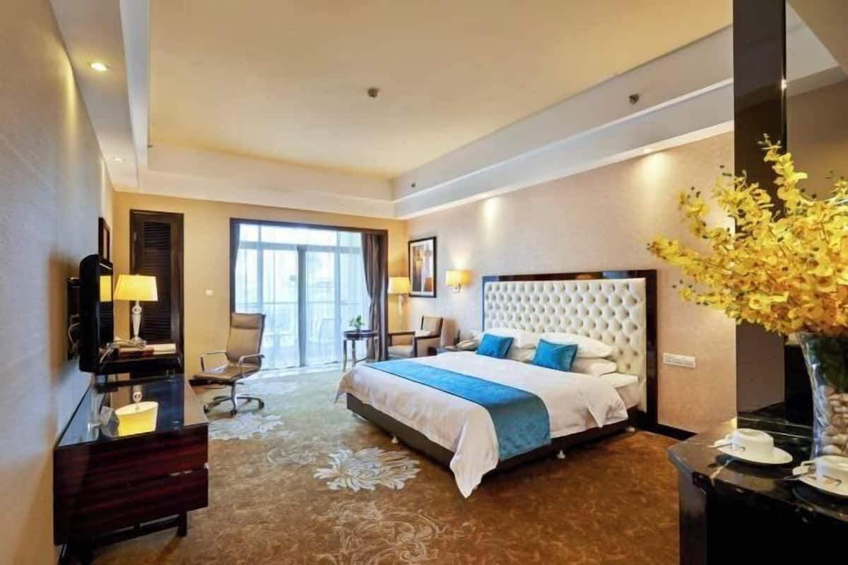 A hotel room with a large bed, a desk with a lamp, a chair, and a vase of flowers.