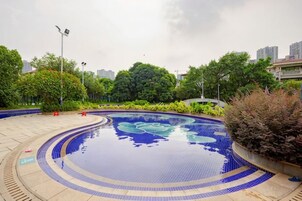 Una piscina con borde de azulejos, rodeada de vegetación y un camino pavimentado.