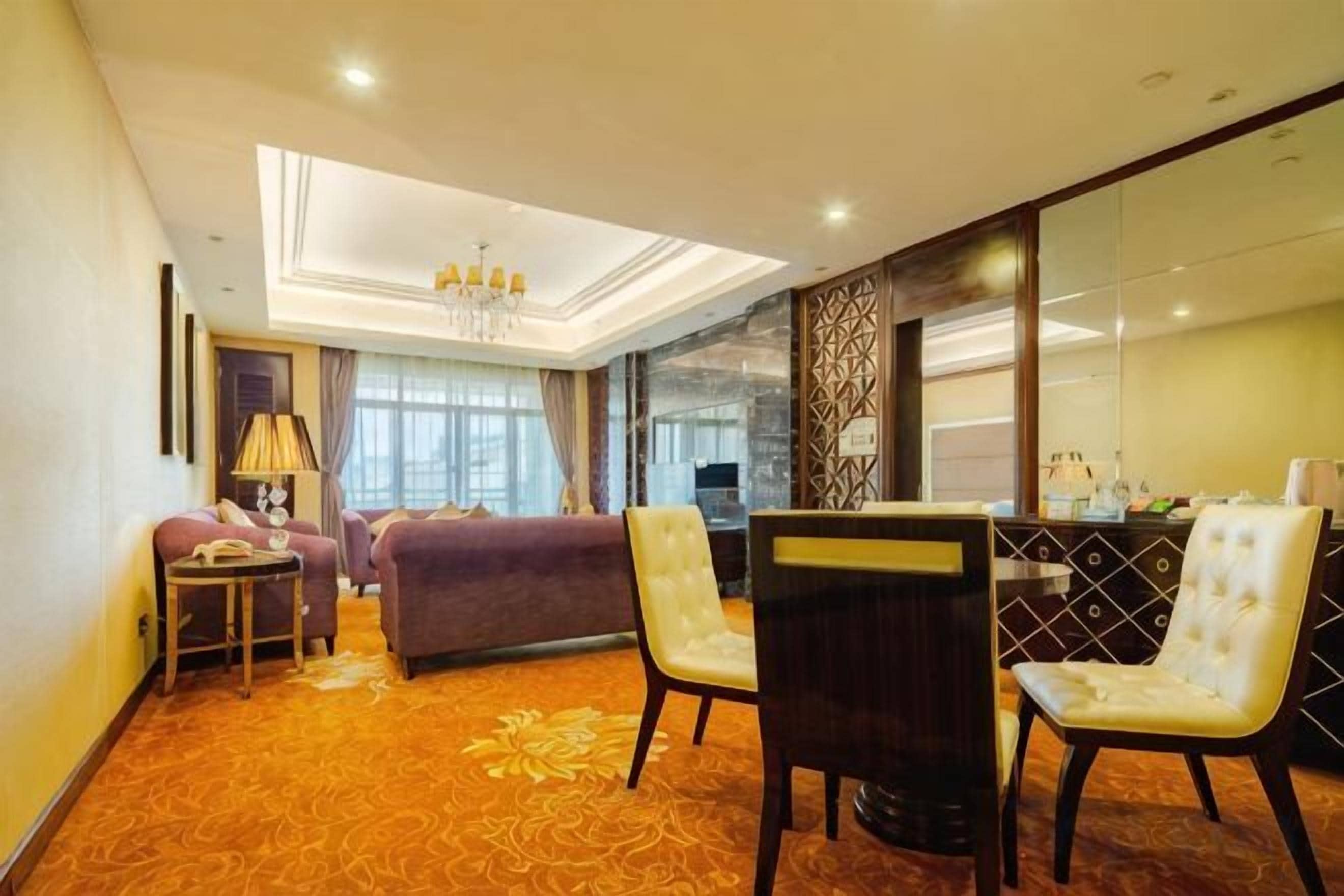 Quarto de hotel com sofá, cadeiras, mesa pequena e espelho decorativo.