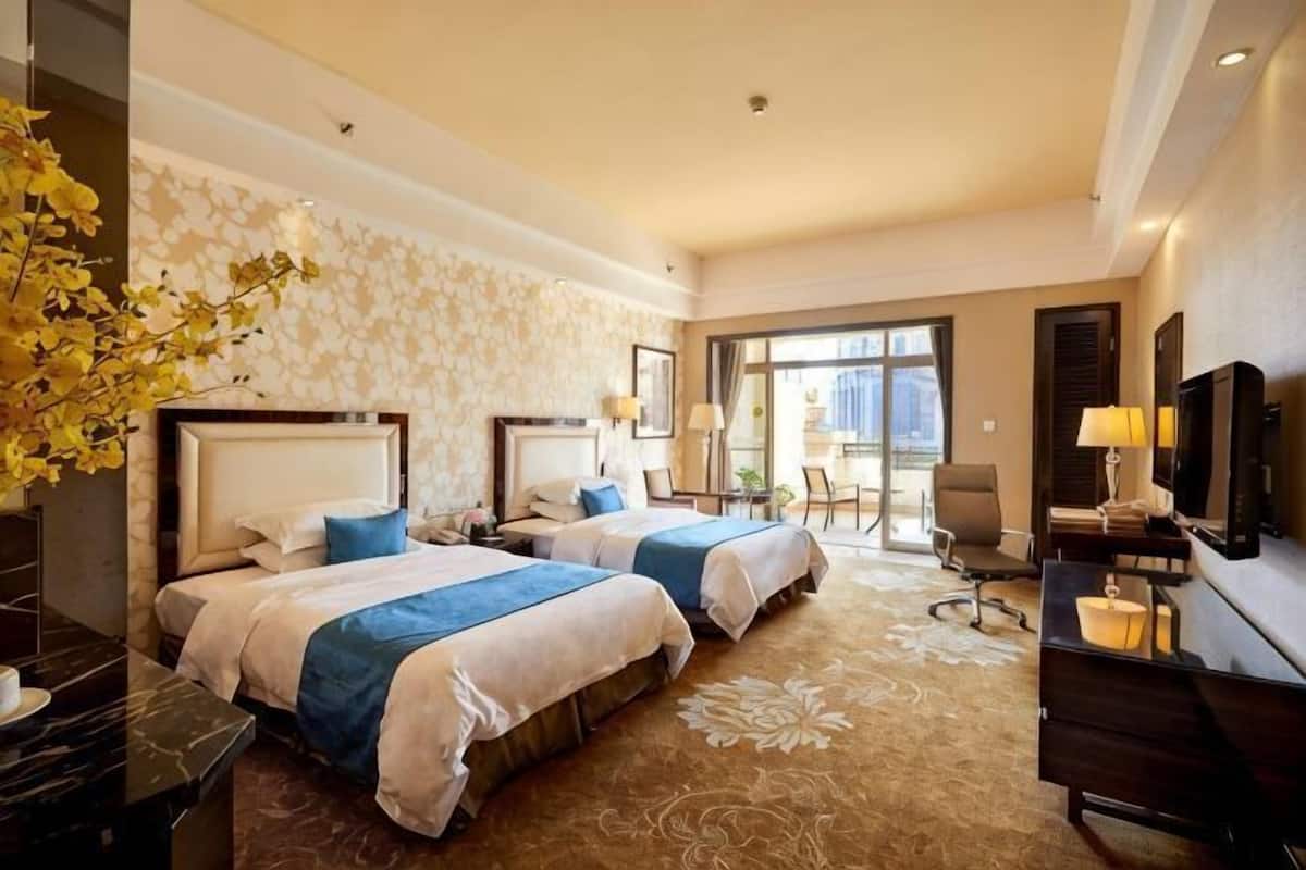 A hotel room with two beds, a desk, a chair, a TV, and a large window.