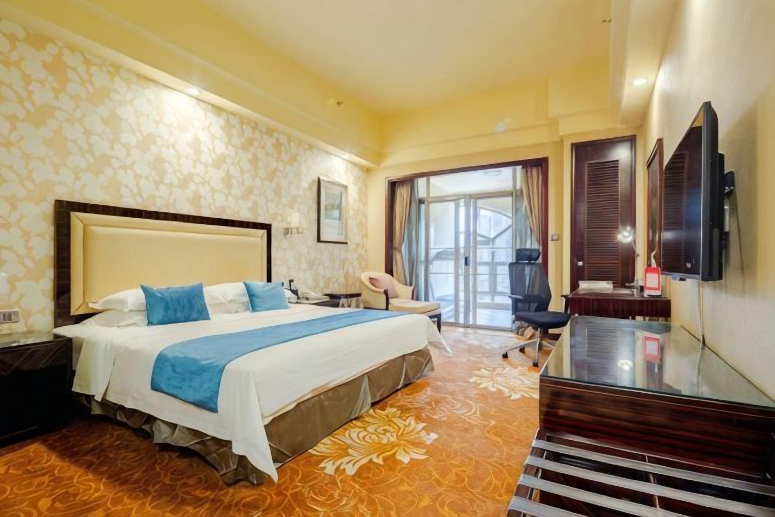 A hotel room with a large bed, a desk, a chair, a television, and a view of the outdoors.