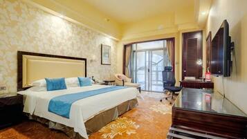 A hotel room with a large bed, a desk, a chair, a television, and a view of the outdoors.