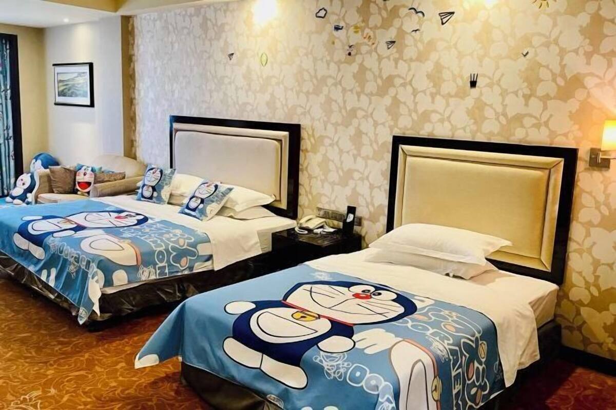 Two hotel beds with cartoon-themed bedding, a nightstand with a phone, and a patterned wall.