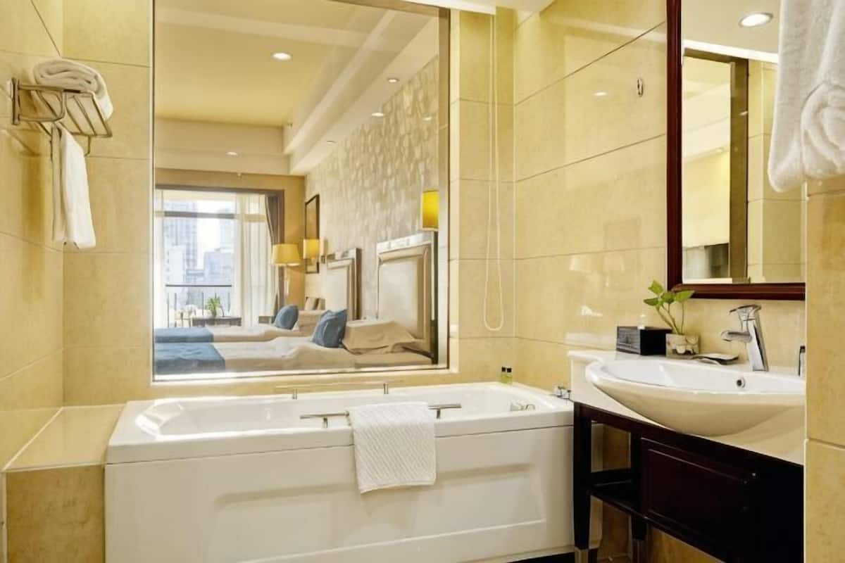 A modern bathroom with a large mirror, a bathtub, a sink, and a view of a bedroom.
