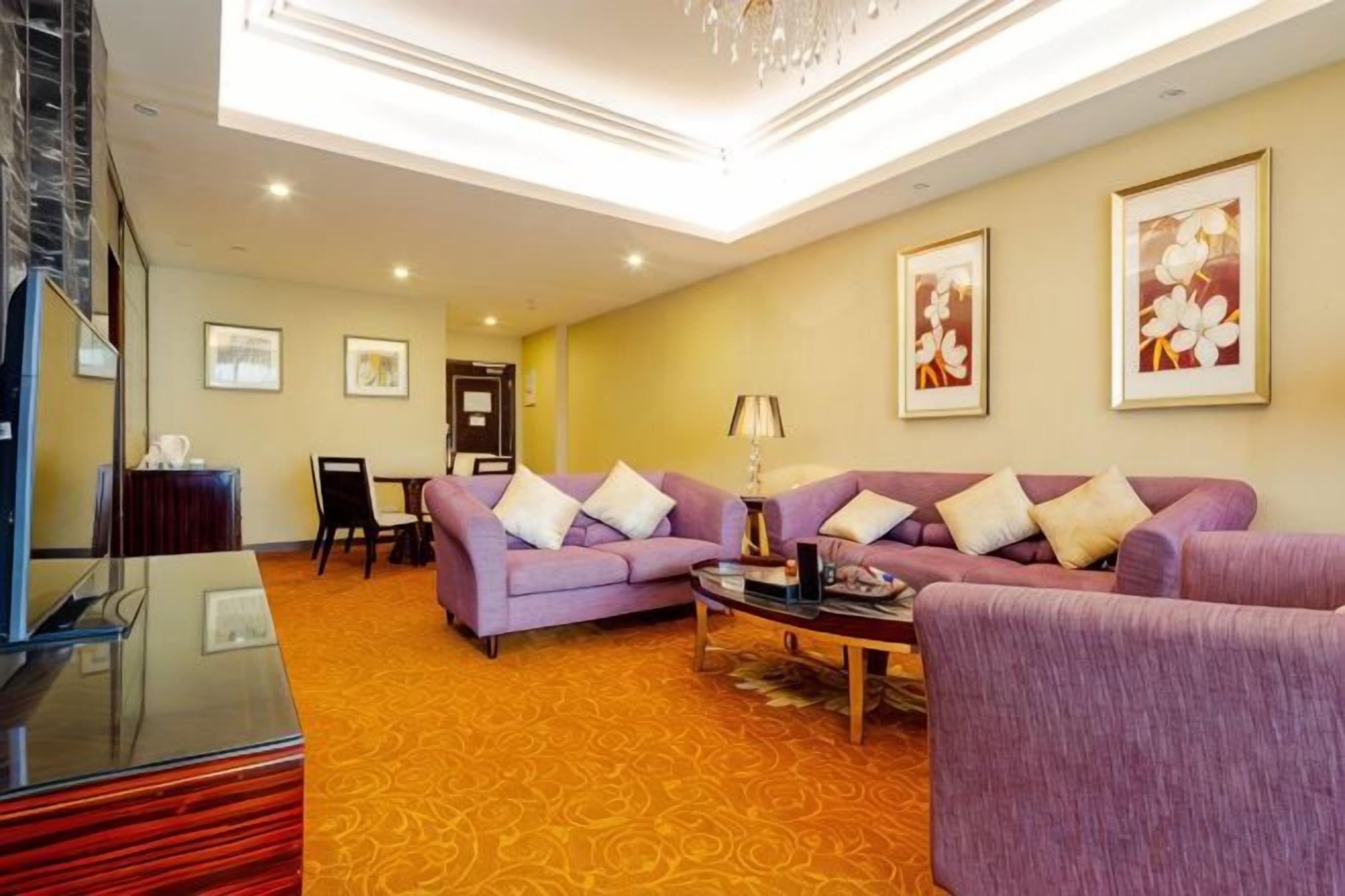 A hotel room with a sofa set, a coffee table, a TV, and artwork on the walls.