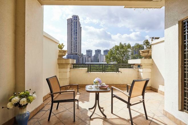 A balcony with two chairs and a table, a vase of flowers, and a view of tall buildings.