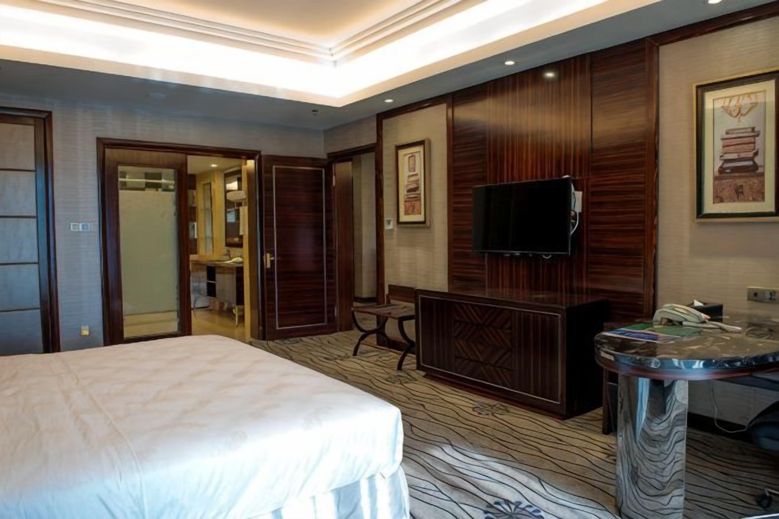 Una camera d'albergo con un letto, una televisione, una scrivania e un bagno visibile attraverso una porta aperta.