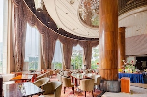 Un comedor amplio con techos altos, ventanas grandes y una columna central. Mesas y sillas dispuestas para comer.