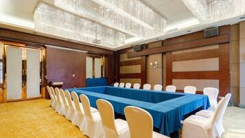 A conference room with a long table, white chairs, and a chandelier.