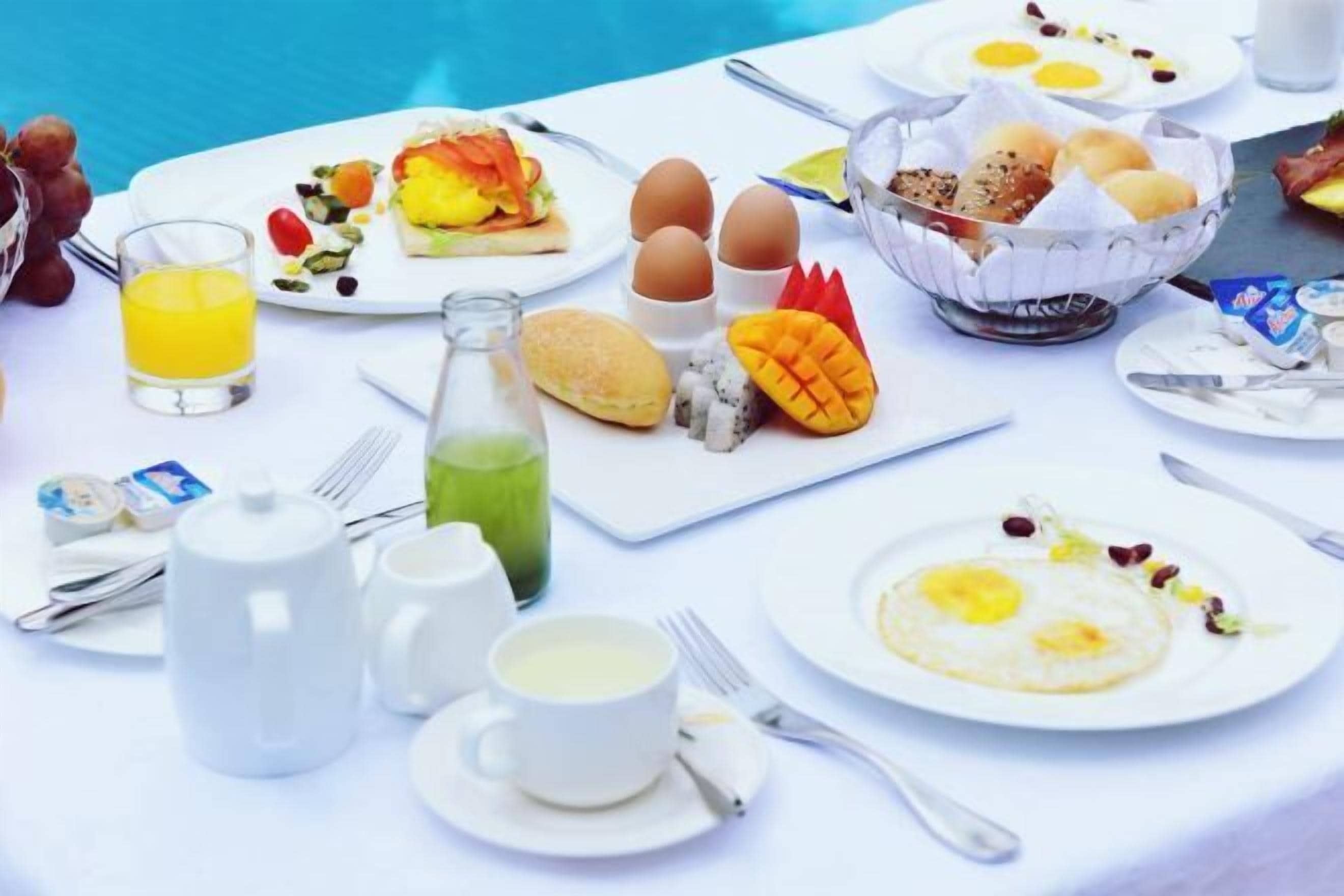 A breakfast setting with various dishes, including eggs, toast, and fruit, along with beverages and utensils.