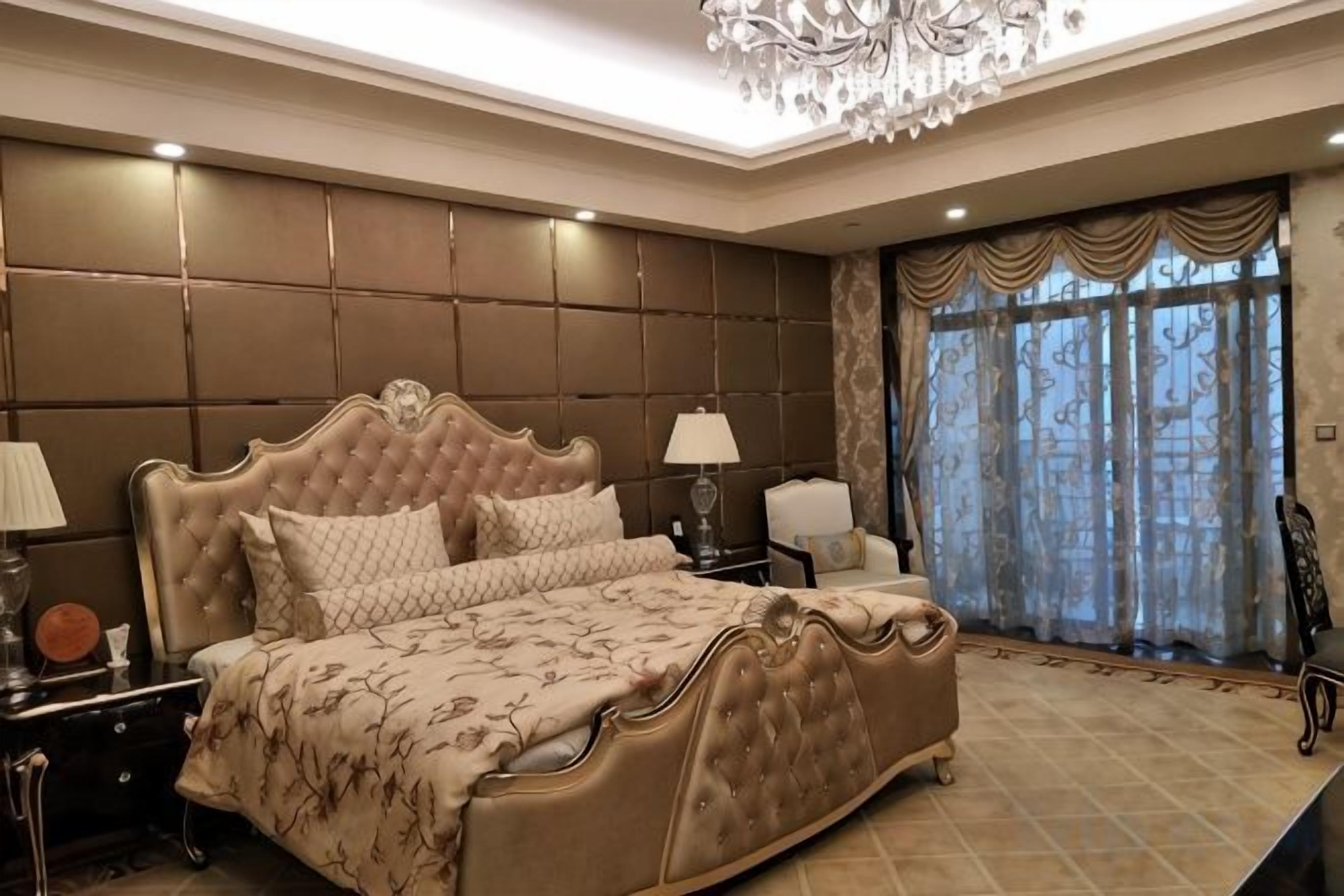 A bedroom with a large bed, a chandelier, and a view through a window with curtains.