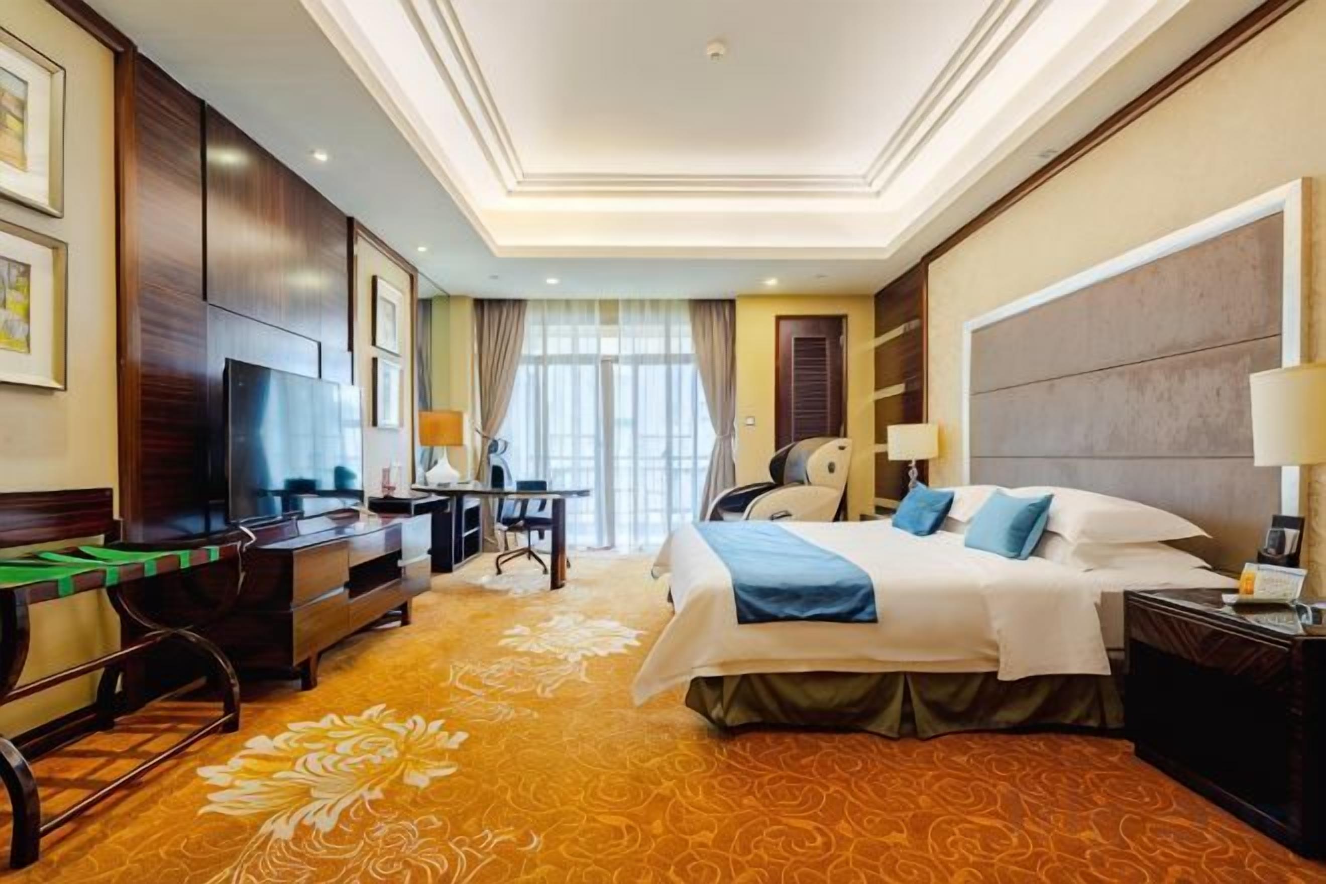 A hotel room with a bed, desk, chair, and a television.