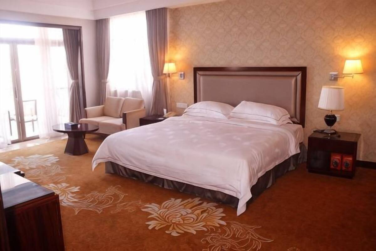 A hotel room with a large bed, a chair, a small table, and a lamp.