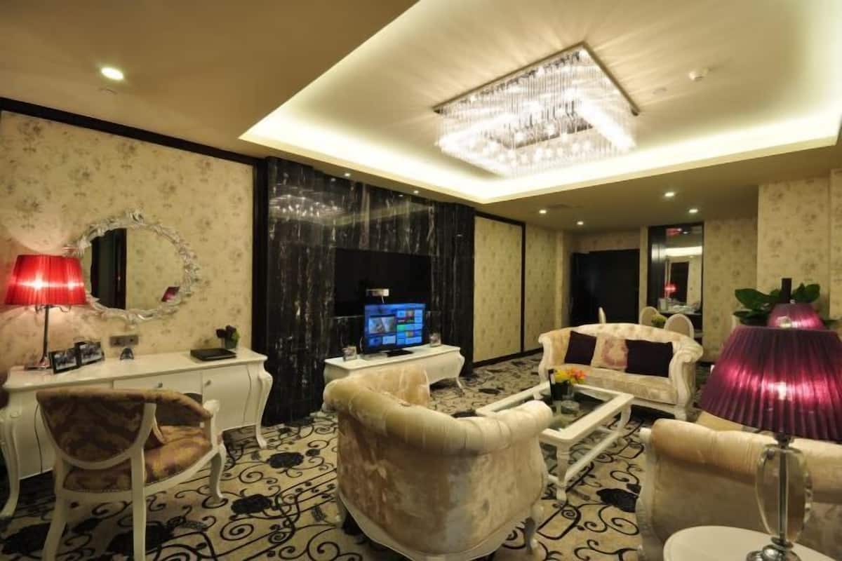 A hotel room with a chandelier, a television, a white desk, a sofa, and a coffee table.