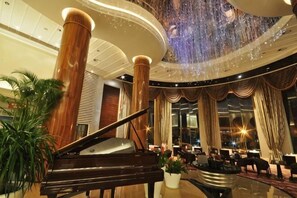 A grand lobby with a grand piano, large columns, and a high ceiling with a decorative light fixture.
