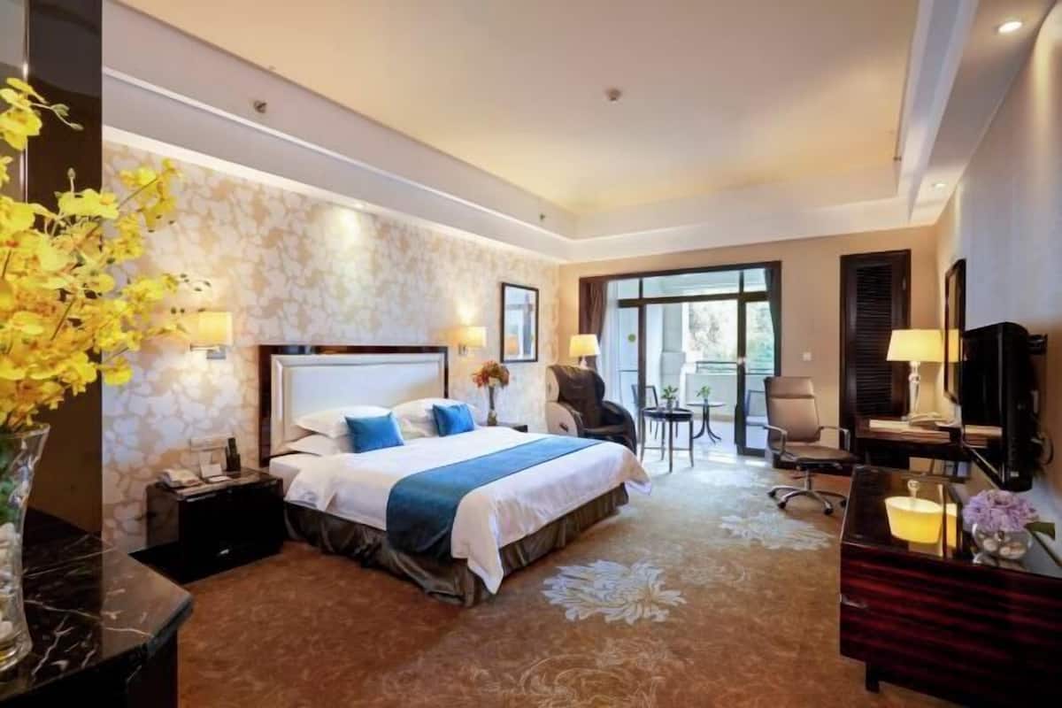 A hotel room with a large bed, a desk, a chair, a TV, and a window.