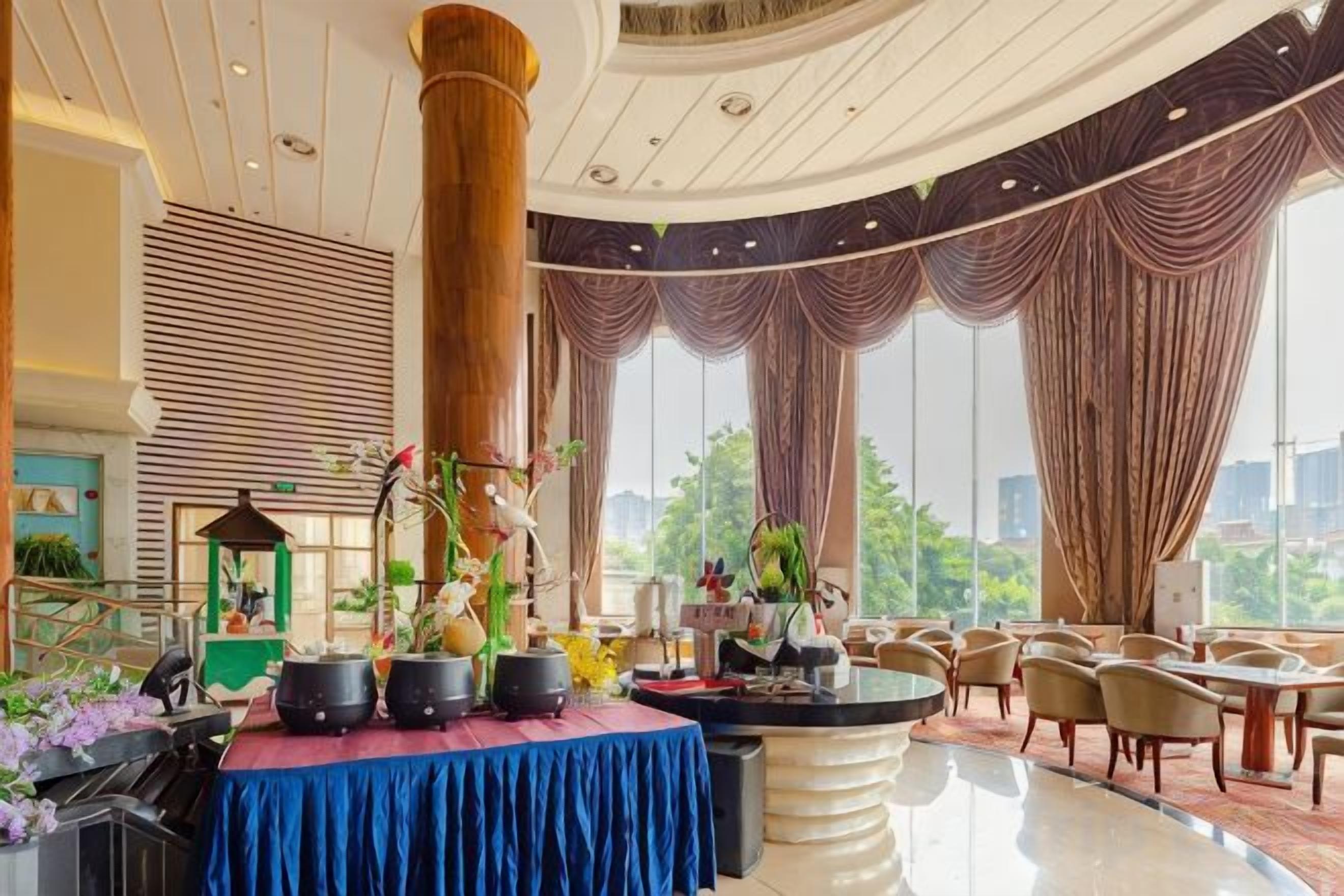 A hotel lobby with a central round table, seating area, and large windows.