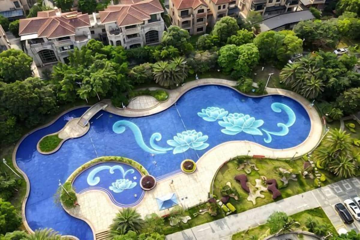 An aerial view of a landscaped swimming pool with floral designs, surrounded by greenery and residential buildings.