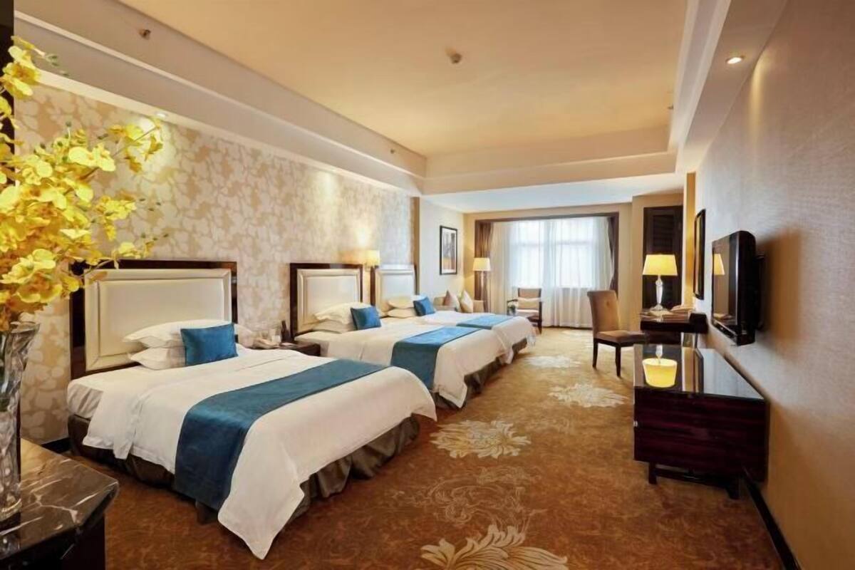 A hotel room with three beds, a TV, a desk, and a vase with flowers.
