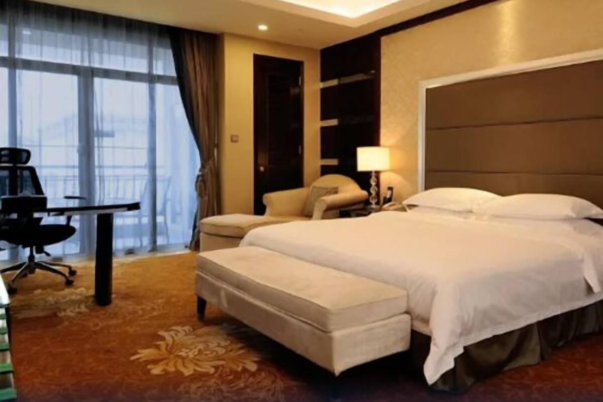 A hotel room with a bed, a desk, a chair, and a large window.