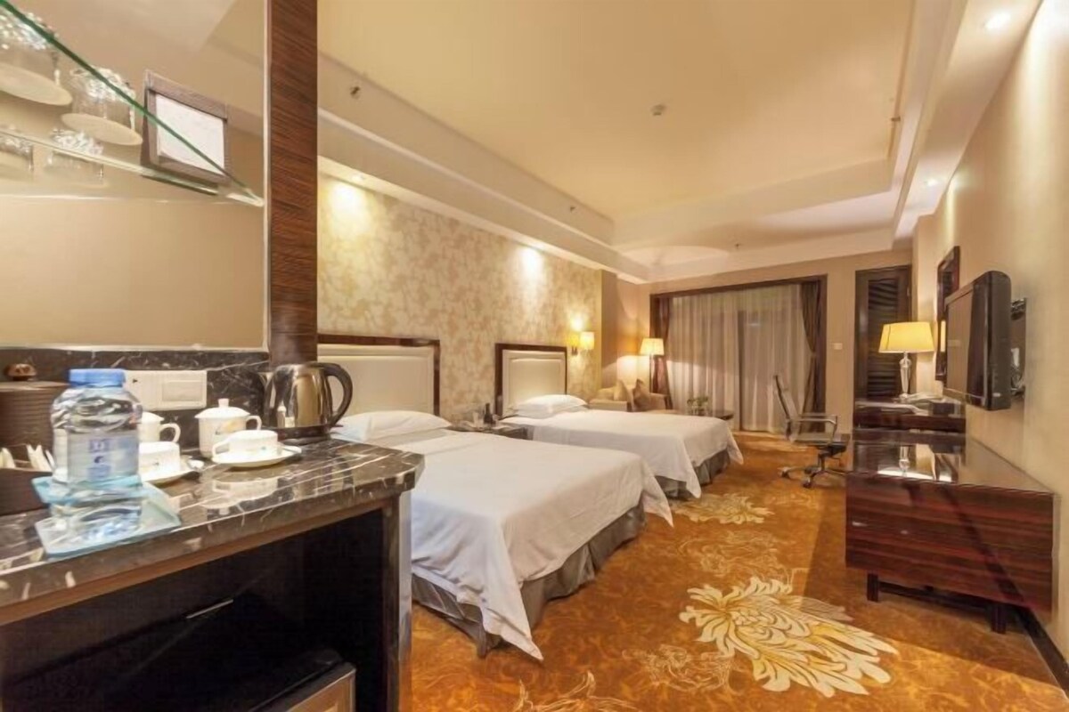 A hotel room with two beds, a desk with a kettle, a coffee maker, and a water bottle.