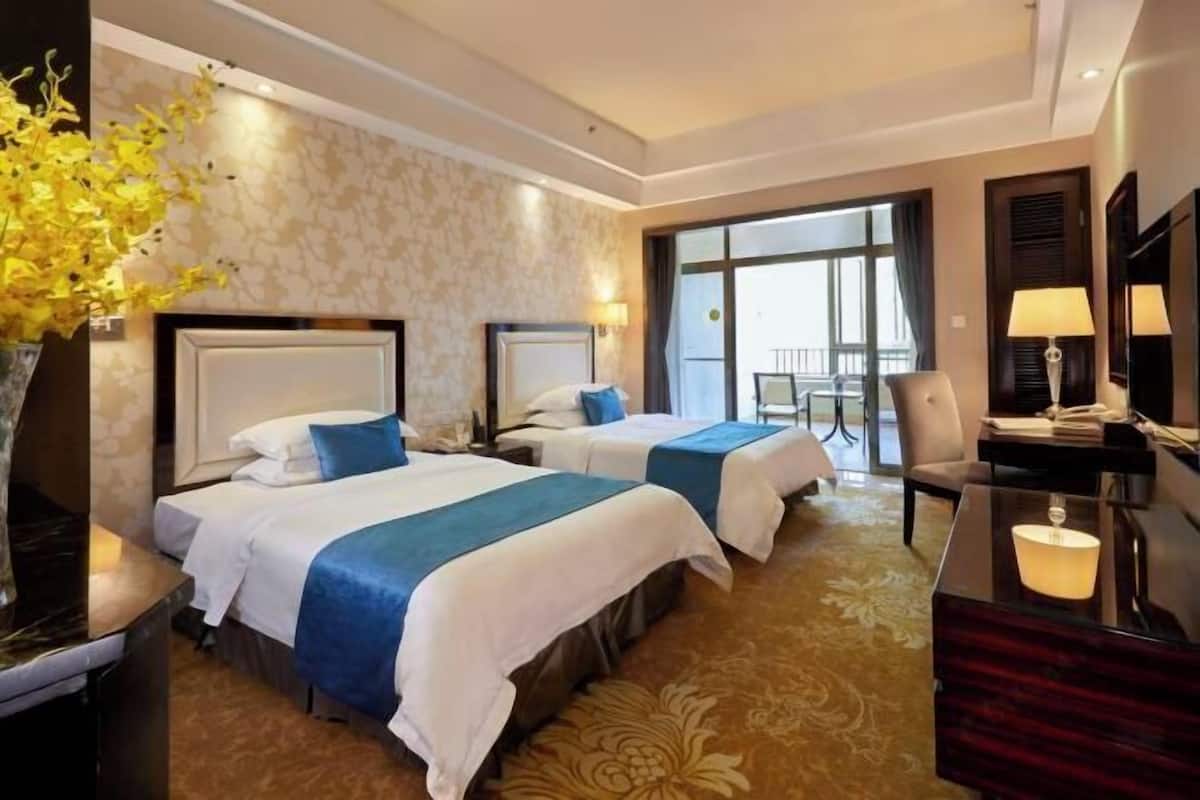 A hotel room with two beds, a desk, a chair, a TV, and a large window.