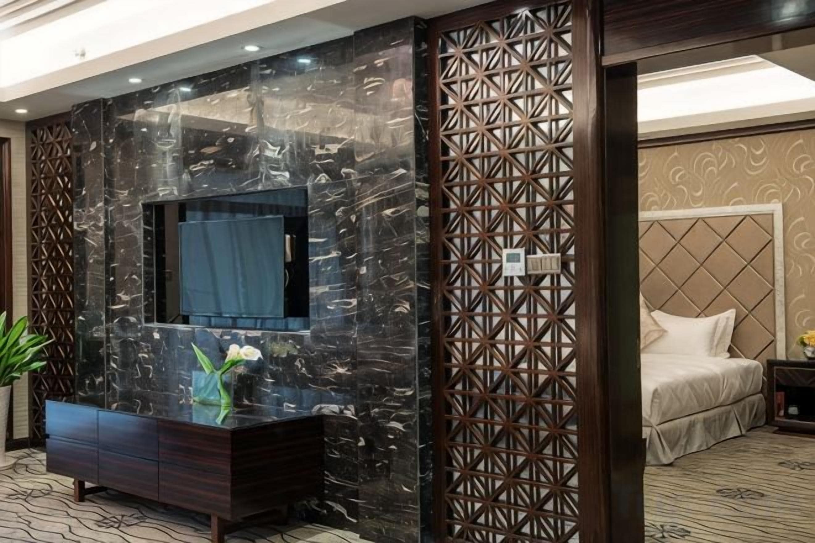 Habitación de hotel con pared de mármol oscuro, un espejo grande, una cama con cabecera y un separador decorativo.